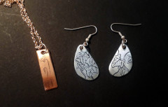 Photo d'un pendentif en cuivre gravé représentant une fleur de cyclamen et d'une paire de boucle d'oreilles en zinc gravé de feuilles de lierre